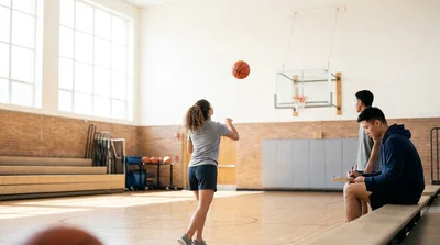 A basketball heading to a hoop in a sunlit gym beside a tally sheet of made and missed shots