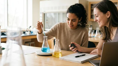 Two clear flasks on a lab bench with a stopwatch and notebook nearby in soft daylight